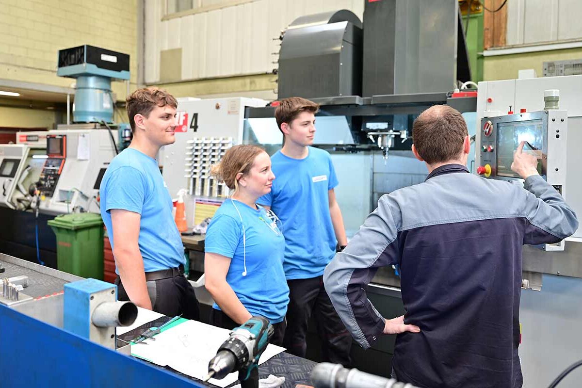 Ausbildner zeigt Lernenden das Bedienen einer Maschine.